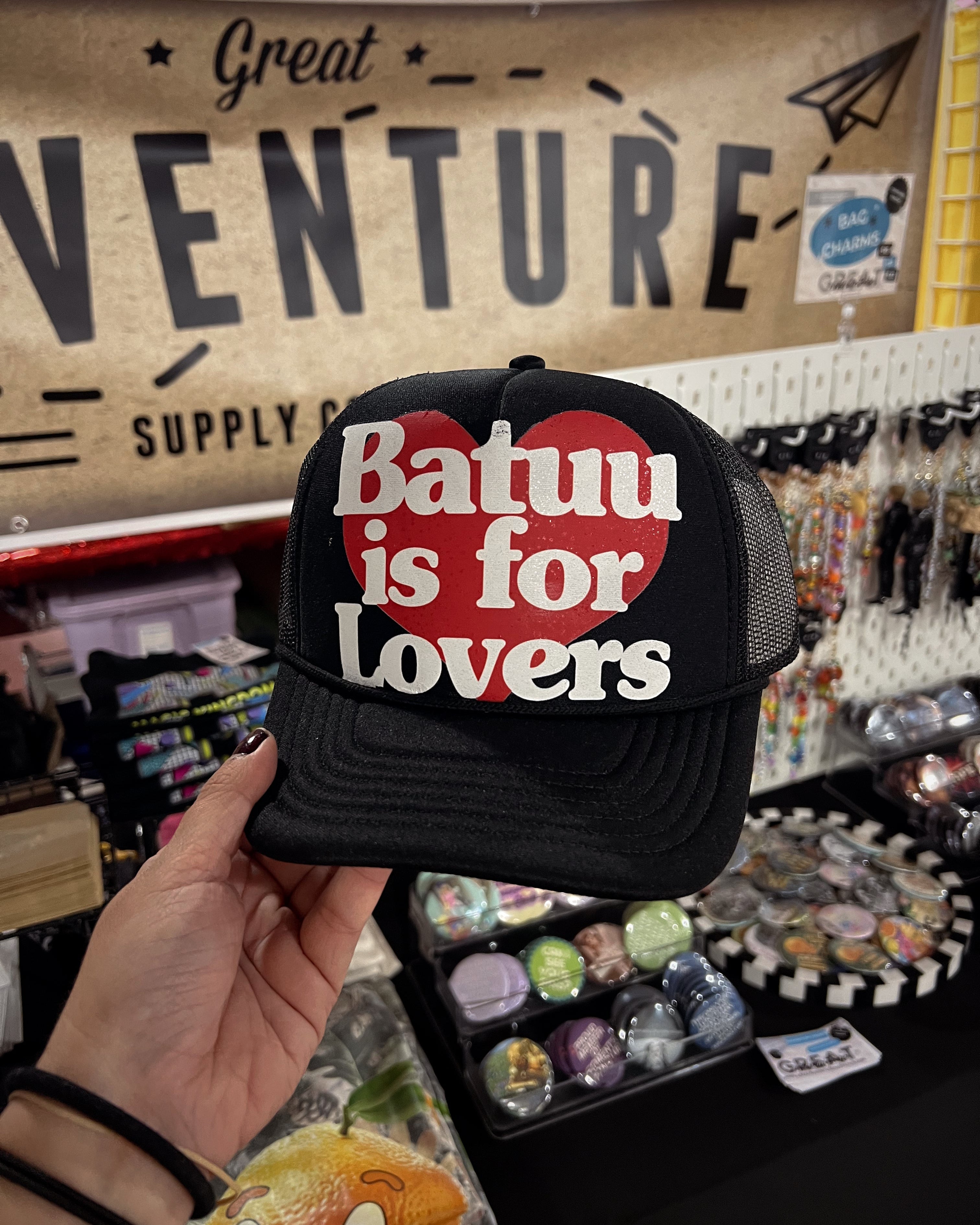 Black cap with 'Batuu is for lovers' text held in front of a store shelf.